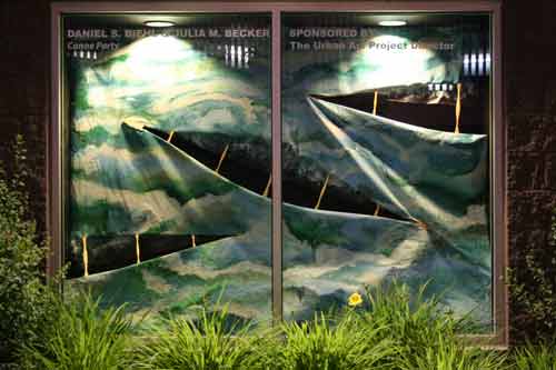 Image of an installation in a display window, featuring 
three canoe-like forms in a whitewater-like painted canvas.